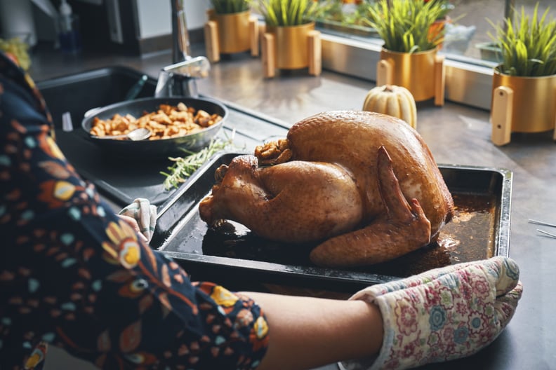 Someone wearing a floral top and floral oven mitts sets roasted turkey on the counter.