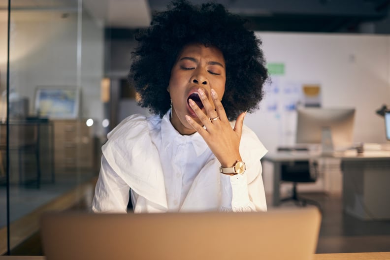 Businesswoman yawning with a laptop sitting in a dark office. 