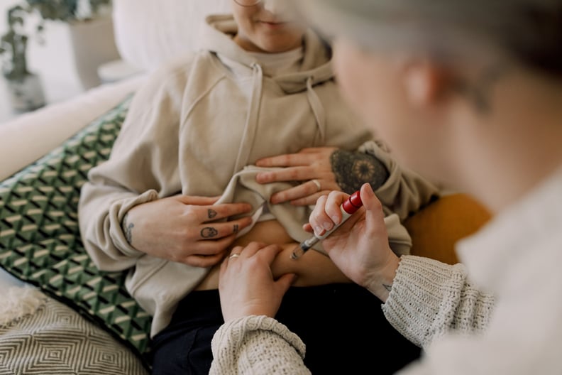 Woman getting fertility treatment at home while sitting down and wearing a beige hoodie and black pants.
