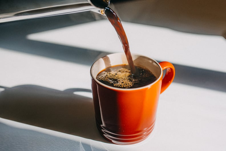 Coffee being poured into an orange mug on a white countertop. 